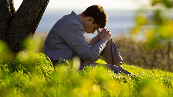 Joven orando a Dios en la naturaleza inclinando su cabeza de rodillas, concepto de religión — Foto de Stock