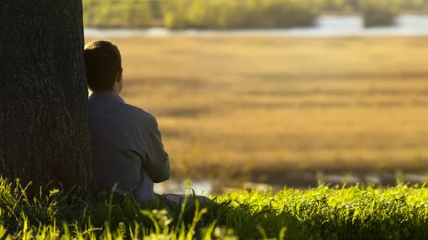 Giovane seduto con la schiena all'albero e meditando sulla vita, il concetto di religione e di riposo — Foto Stock