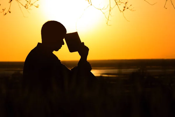Silhouette d'un jeune homme avec une Bible, homme priant Dieu dans la nature, le concept de religion et de spiritualité — Photo