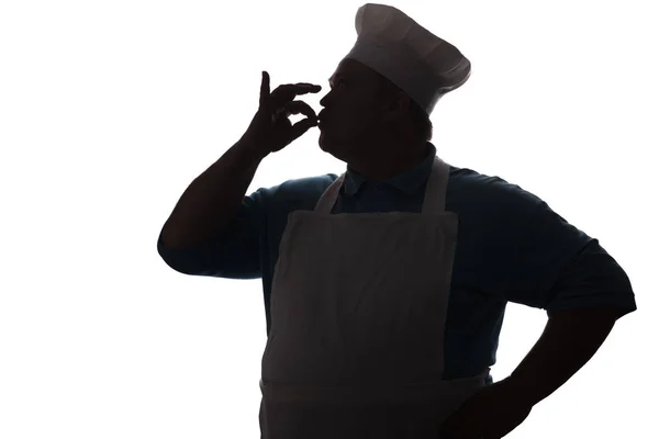 Silhouette of a happy chef kissing fingers out of delicious dishes, a person's profile in a kitchen uniform showing ok by hand — Stock Photo, Image