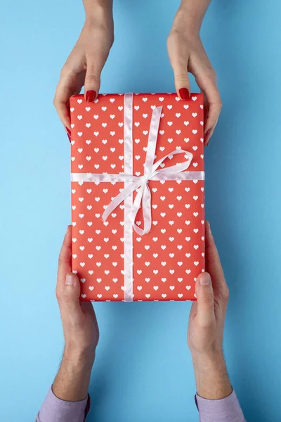 Homem dá uma menina um presente de mão em mão, caixa envolta em papel decorativo com um fundo laranja arco, o conceito de feriados, amor e relacionamentos, vista superior — Fotografia de Stock