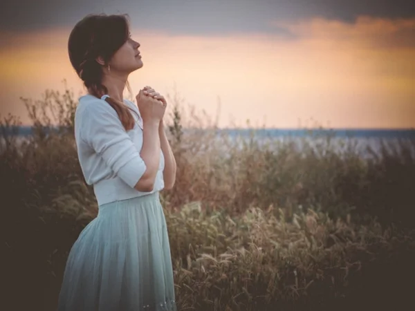 silhouette profile of a beautiful girl in a dress praying to God in the field, a young woman walking on nature during sunset looking up into the sky, religion concept