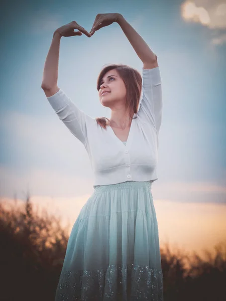 Bella ragazza nel campo ha piegato le mani a forma di cuore, una giovane ragazza che cammina, il concetto di bellezza, natura, gioventù, amore e sentimenti — Foto Stock