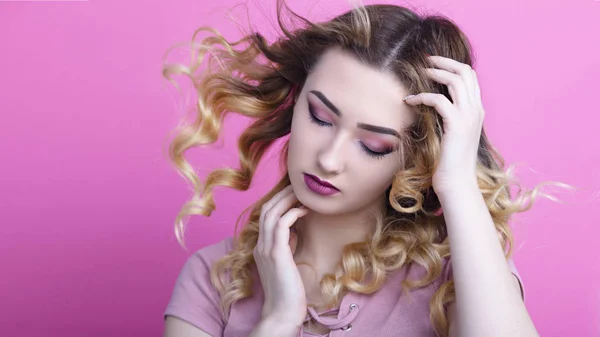 porter of a beautiful girl on a pink studio background with curled hair and makeup, the concept of beauty and youth