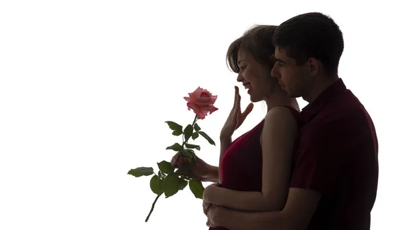 Silhouette of a young man and woman in love on white isolated background, boy came up behind to girl to make a surprise with rose flower, concept romantic, holidays — Stock Photo, Image