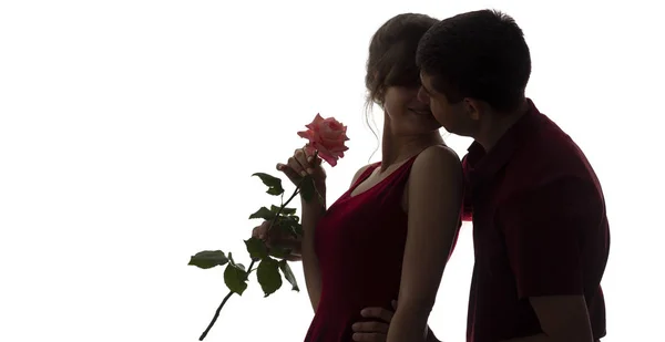 Silhouette of a young man and woman fall in love on white isolated background, boy came up behind to girl to make a surprise with rose flower and kisses cheek, concept romantic, — Stock Photo, Image