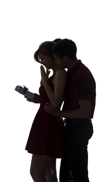 Silhouette of a young couple in love on white isolated background, man came up behind to woman to make a surprise with box present, concept romantic holidays — Stock Photo, Image