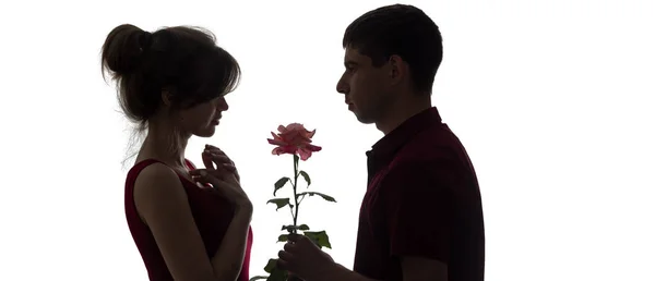 Perfil silueta de una joven pareja enamorada sobre fondo blanco aislado, hombre dando a una mujer una flor de rosa, concepto amor y romance —  Fotos de Stock