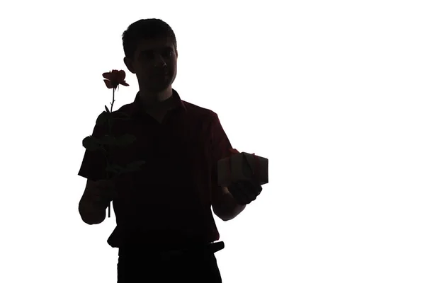 Silhouet van de jonge man met een geschenkdoos en een roos bloem voor zijn geliefde, jongen feliciteert op witte geïsoleerde achtergrond, concept Holidays, zorg, liefde, romantiek — Stockfoto