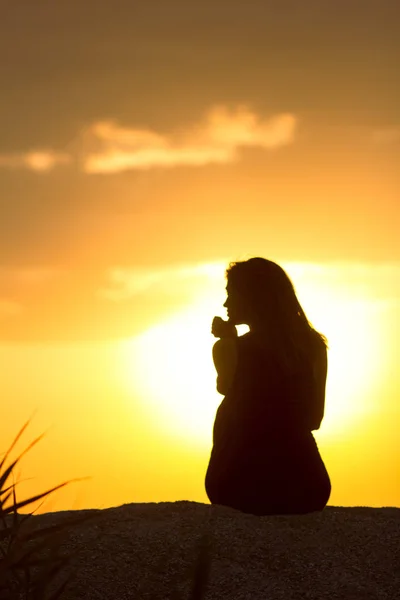 Silhouette di bella ragazza premurosa seduta sulla sabbia e godersi il tramonto, la figura della giovane donna sulla spiaggia, meditare femminile sulla natura — Foto Stock