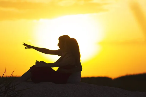 Silhouette di una coppia amorevole al tramonto seduta sulla sabbia sulla spiaggia, profilo di un uomo e una donna innamorati che fissano un obiettivo, una scena romantica nella natura, riposo estivo — Foto Stock