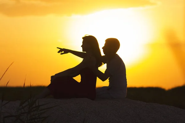 Silhouette of a loving couple at sunset sitting on sand on the beach, profile of a man and a woman in love staring ahead at one goal, a romantic scene in nature, summer rest — Stock Photo, Image