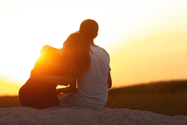 Silhueta de um casal amoroso ao pôr do sol sentado na areia na praia, a figura de um homem e uma mulher apaixonada, uma cena romântica na natureza, umas férias em família, descanso de verão — Fotografia de Stock