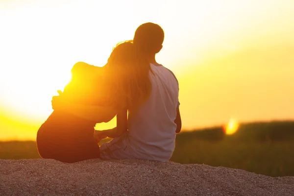 Silhouette of a loving couple at sunset sitting on sand on the beach, the figure of a man and a woman in love, a romantic scene in nature, a family vacation, summer rest — Stock Photo, Image