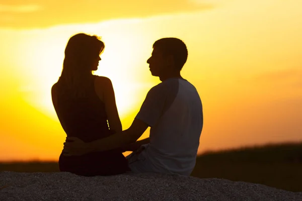 Silhueta de um casal amoroso ao pôr do sol sentado na areia na praia, a figura de um homem e uma mulher apaixonada, uma cena romântica na natureza, umas férias em família, descanso de verão — Fotografia de Stock