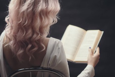 sarışın kız bir sandalyede oturan açık kitap tutan, bir roman okuma genç kadının arka, hobi kavramı, gevşeme, siyah arka plan üzerinde eğlence