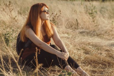 omuzlarında bir sırt çantası ile genç kız bir alanda oturan ve gün batımı zevk, yürüyüş kavramı, yürüyüş, dinlenme, aktif yaşam tarzı