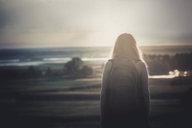 omuzlarında bir sırt çantası ile genç kız bir alanda oturan ve gün batımı zevk, yürüyüş kavramı, yürüyüş, dinlenme, aktif yaşam tarzı