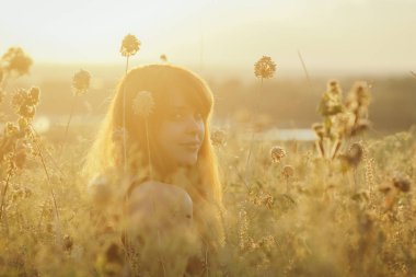rüya gibi kızıl saçlı kız kurutulmuş çiçekler arasında bir alanda yere oturur ve gün batımında doğa sahiptir, genç kadın rahatlatıcı, dinlenme kavramı, sağlık, uyum, yaşam tarzı
