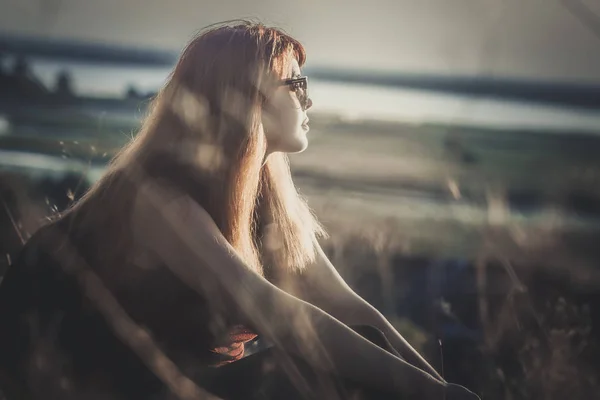Silhouette di una giovane ragazza con uno zaino sulle spalle che cammina in un campo e al tramonto, concept trekking, passeggiate, riposo, vita attiva — Foto Stock