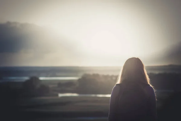 Joven con una mochila sobre sus hombros sentada en un campo y disfrutando de la puesta de sol, concepto de senderismo, caminar, descansar, estilo de vida activo —  Fotos de Stock