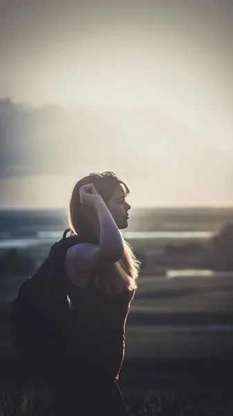 Jeune fille avec un sac à dos sur les épaules assis dans un champ et profiter du coucher du soleil, concept de randonnée, marche, repos, mode de vie actif — Photo