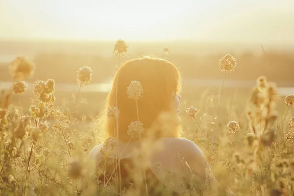 Cabeça para trás de menina ruiva sentada no chão em um campo entre flores secas e gosta da natureza ao pôr do sol, jovem relaxante, conceito de descanso, cuidados de saúde, harmonia, estilo de vida — Fotografia de Stock