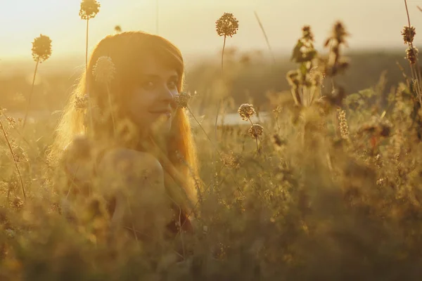 Мечтательная рыжеволосая девушка сидит на земле в поле среди сушеных цветов и наслаждается природой на закате, молодая женщина расслабляется, концепция отдыха, здравоохранения, гармонии, образа жизни — стоковое фото