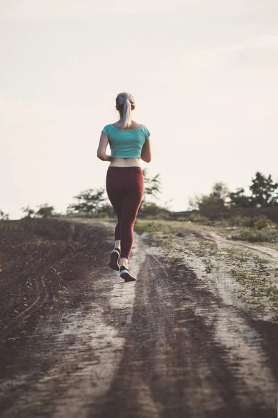 Schienale di giovane donna in abbigliamento sportivo corsa distanza nel campo, ragazza impegnata nello sport all'aria aperta, concetto di stile di vita sano — Foto Stock