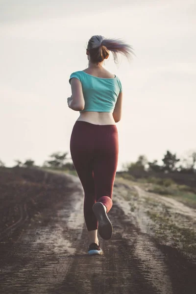 Schienale di giovane donna in abbigliamento sportivo corsa distanza nel campo, ragazza impegnata nello sport all'aria aperta, concetto di stile di vita sano — Foto Stock