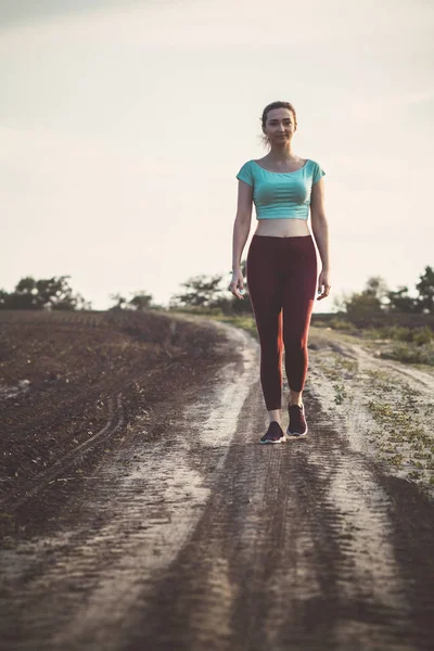 Young woman in sportswear walks along path in the field, concept of sports and healthy lifestyle — Stock Photo, Image