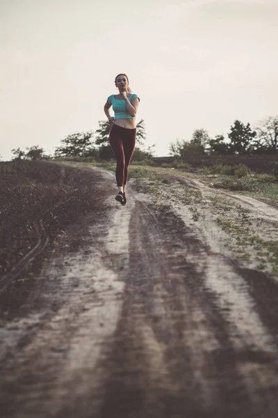 Giovane donna in abbigliamento sportivo distanza di corsa sul campo, ragazza impegnata nello sport all'aperto in una giornata nuvolosa, concetto di stile di vita sano e cura del corpo — Foto Stock