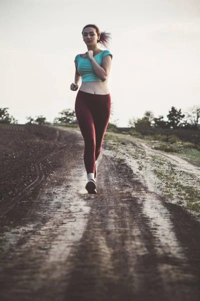Giovane donna in abbigliamento sportivo distanza di corsa sul campo, ragazza impegnata nello sport all'aperto in una giornata nuvolosa, concetto di stile di vita sano e cura del corpo — Foto Stock