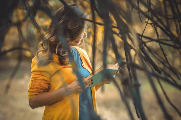 Hermosa chica leyendo libro en el bosque de otoño, mujer joven caminando en soledad en la naturaleza, concepto hobby y estilo de vida — Foto de Stock