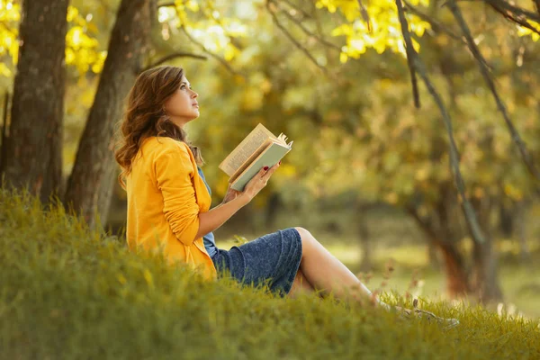 Herfst portret van een mooi meisje zittend op de helling met een open boek, vrouw lezing roman over de natuur, concept hobby en lifestyle — Stockfoto