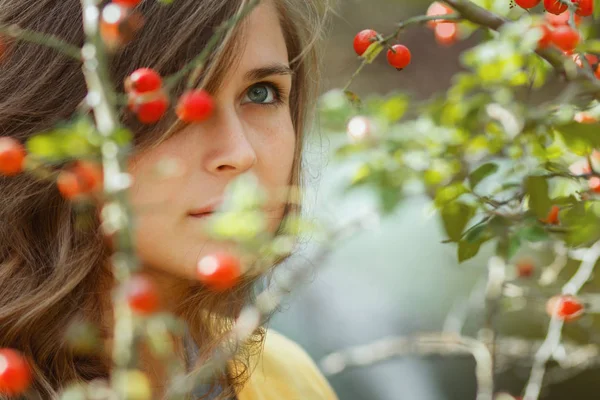 Retrato de outono de uma jovem pensativa por trás dos ramos de um arbusto de rosa mosqueta com bagas vermelhas, bela cara de menina com um olhar adulto pensativo para cima — Fotografia de Stock