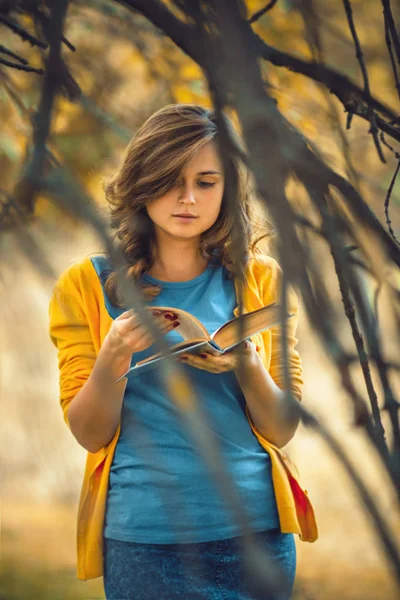 Retrato de otoño de una hermosa chica con un libro abierto en las ramas desnudas, una mujer lee ficción sobre la naturaleza, el concepto hobby y el estilo de vida — Foto de Stock