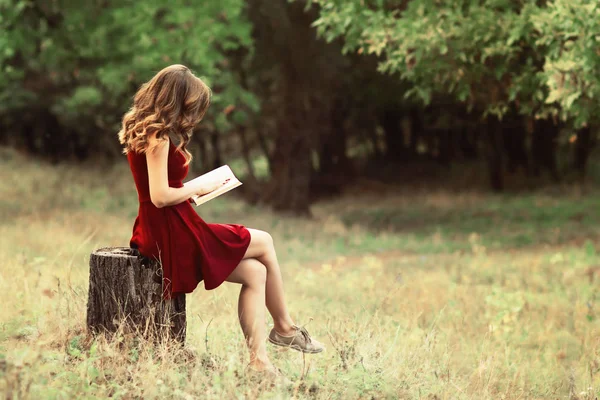 Perfil de mujer joven con libro abierto en las manos sentado en un tocón de árbol, en un claro bosque mujer leyendo novela sobre la naturaleza, el concepto hobby y el estilo de vida — Foto de Stock