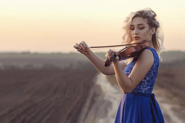 Retrato de una hermosa joven con un violín bajo la barbilla al atardecer, niña tocando un instrumento musical sobre la naturaleza, música conceptual y pasatiempos — Foto de Stock
