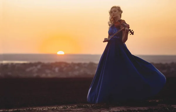 Figura di giovane donna in abito lungo con violino in campo al tramonto, ragazza impegnata nell'arte musicale, performance sulla natura, concetto passione per la musica — Foto Stock