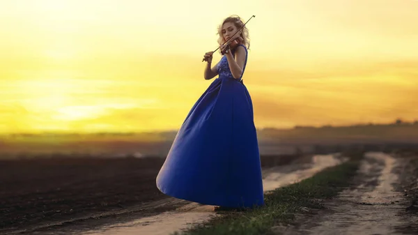 Figura di giovane donna in abito lungo con violino in campo al tramonto, ragazza impegnata nell'arte musicale, performance sulla natura, concetto passione per la musica — Foto Stock