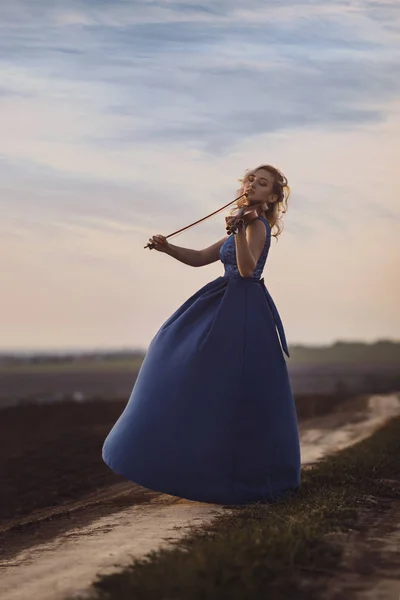 Figura di giovane donna in abito lungo con violino in campo al tramonto, ragazza impegnata nell'arte musicale, performance sulla natura, concetto passione per la musica — Foto Stock