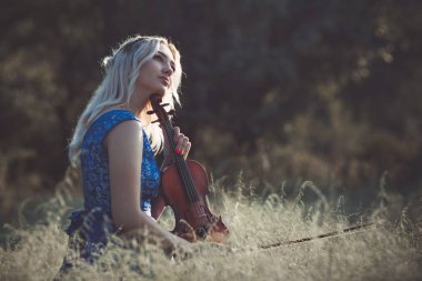 Şafakta çayırda kuru çimenlerde keman çalan ve doğada esinlenerek müzik aleti çalan inanılmaz derecede güzel bir kızın portresi.