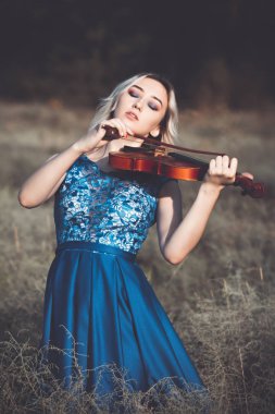 Şafakta çayırda kuru çimenlerde keman çalan ve doğada esinlenerek müzik aleti çalan inanılmaz derecede güzel bir kızın portresi.