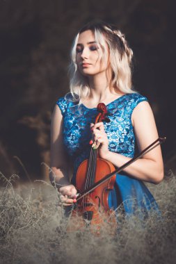 Şafakta çayırda kuru çimenlerde keman çalan ve doğada esinlenerek müzik aleti çalan inanılmaz derecede güzel bir kızın portresi.