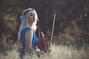 Şafakta çayırda kuru çimenlerde keman çalan ve doğada esinlenerek müzik aleti çalan inanılmaz derecede güzel bir kızın portresi.