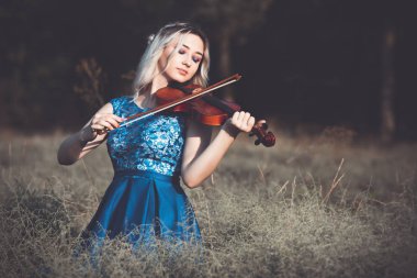 Şafakta çayırda kuru çimenlerde keman çalan ve doğada esinlenerek müzik aleti çalan inanılmaz derecede güzel bir kızın portresi.
