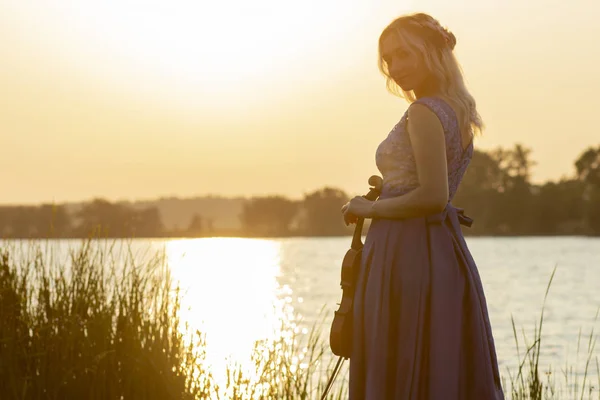 川の岸の夜明けにバイオリンを持つ若い女性のロマンチックなシルエット自然、コンセプト音楽とインスピレーションに楽器を演奏エレガントな女の子 — ストック写真