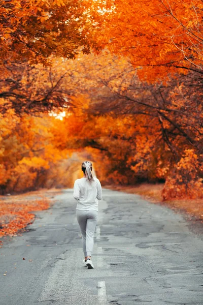 Plecy młodej kobiety w odzieży sportowej na drodze asfaltowej, dziewczyna zaangażowana w sport na świeżym powietrzu w jesienny dzień, koncepcja zdrowego stylu życia i pielęgnacji ciała — Zdjęcie stockowe