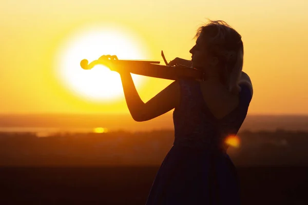 Silueta de una figura femenina tocando la vioylin al atardecer, mujer relajándose en la música clásica, actuación en la naturaleza, concepto de arte sonoro — Foto de Stock